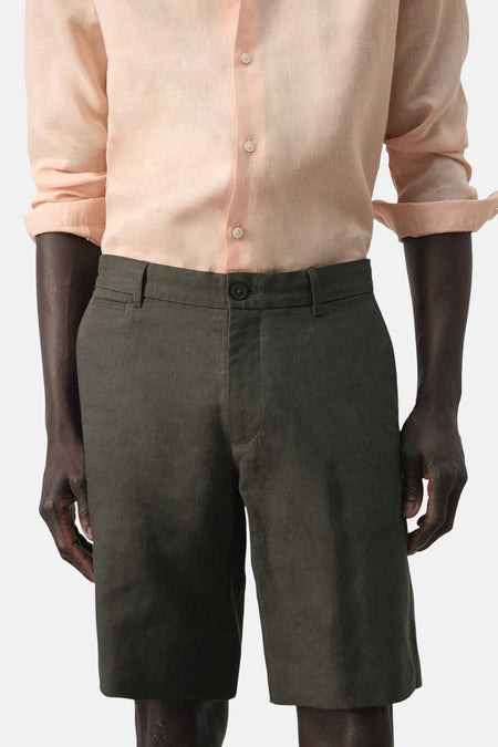 Kaki bermuda van MANGO, met een effen kleur en een relaxte pasvorm, gecombineerd met een perzikkleurig linnen overhemd.
