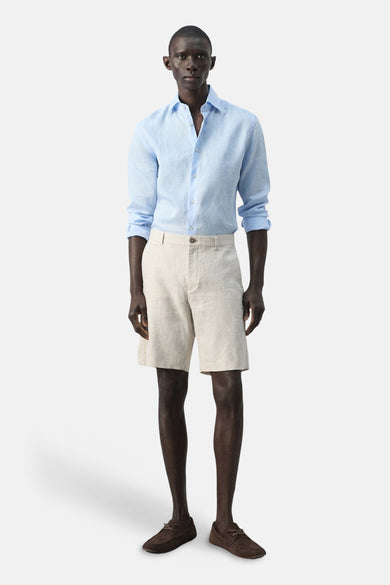 Beige bermuda van MANGO, gecombineerd met een lichtblauw linnen overhemd en bruine mocassins.
