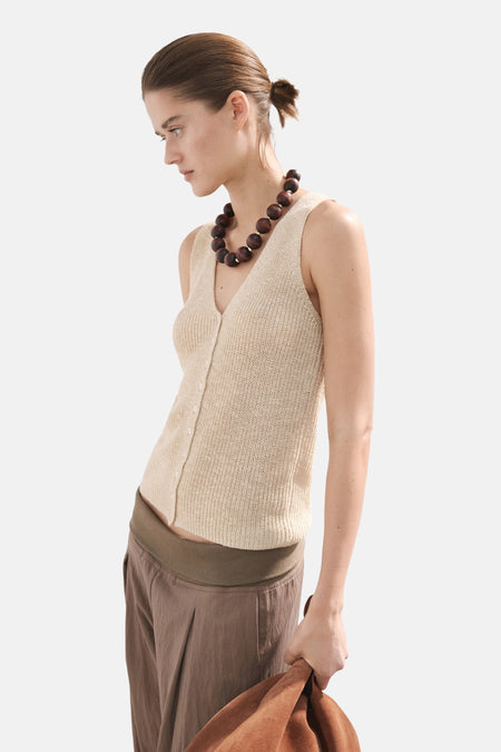 Haut beige sans manches de MANGO, avec fermeture à boutons, texture tricotée et collier de perles en bois.