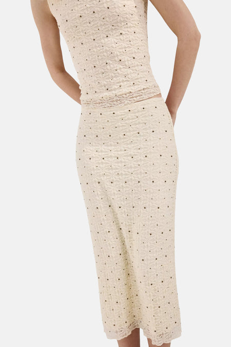Jupe longue écru de MANGO avec motif ajouré et petits clous bronze, portée par un mannequin de dos.