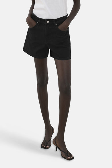 Zwarte short van MANGO, gedragen met een wit shirt en zwarte hakken tegen een witte achtergrond.
