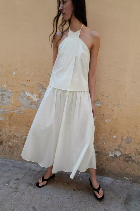 Jupe longue écru de MANGO, plissée avec de fines rayures verticales, portée avec un haut bustier blanc et des sandales noires.