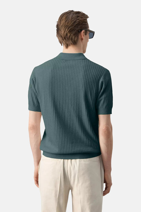 Groene polo van MANGO, geribd met korte mouwen, van achteren gezien op model met lichte broek.