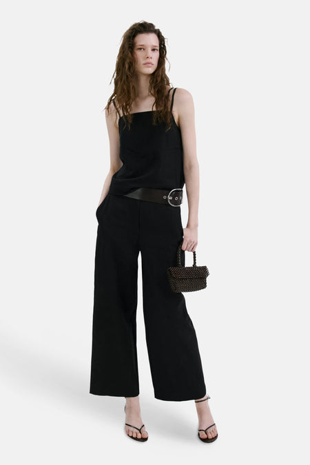 Haut noire à fines bretelles de MANGO, associée à un pantalon large, une ceinture, des sandales et un sac à perles.