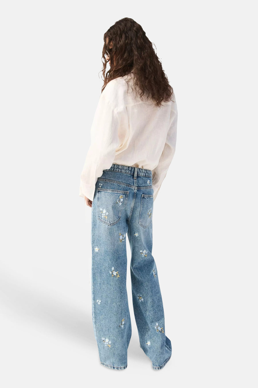 Rechte jeans van lichtblauwe denim van MANGO, met bloemborduursels, aan de achterkant gedragen door een vrouw in wit overhemd.