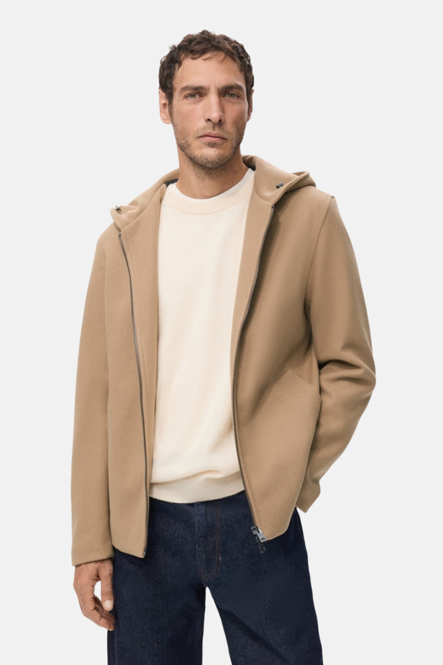 Beige, korte jas van MANGO met capuchon, open rits en gedragen over een crèmekleurige trui en donkerblauwe jeans.