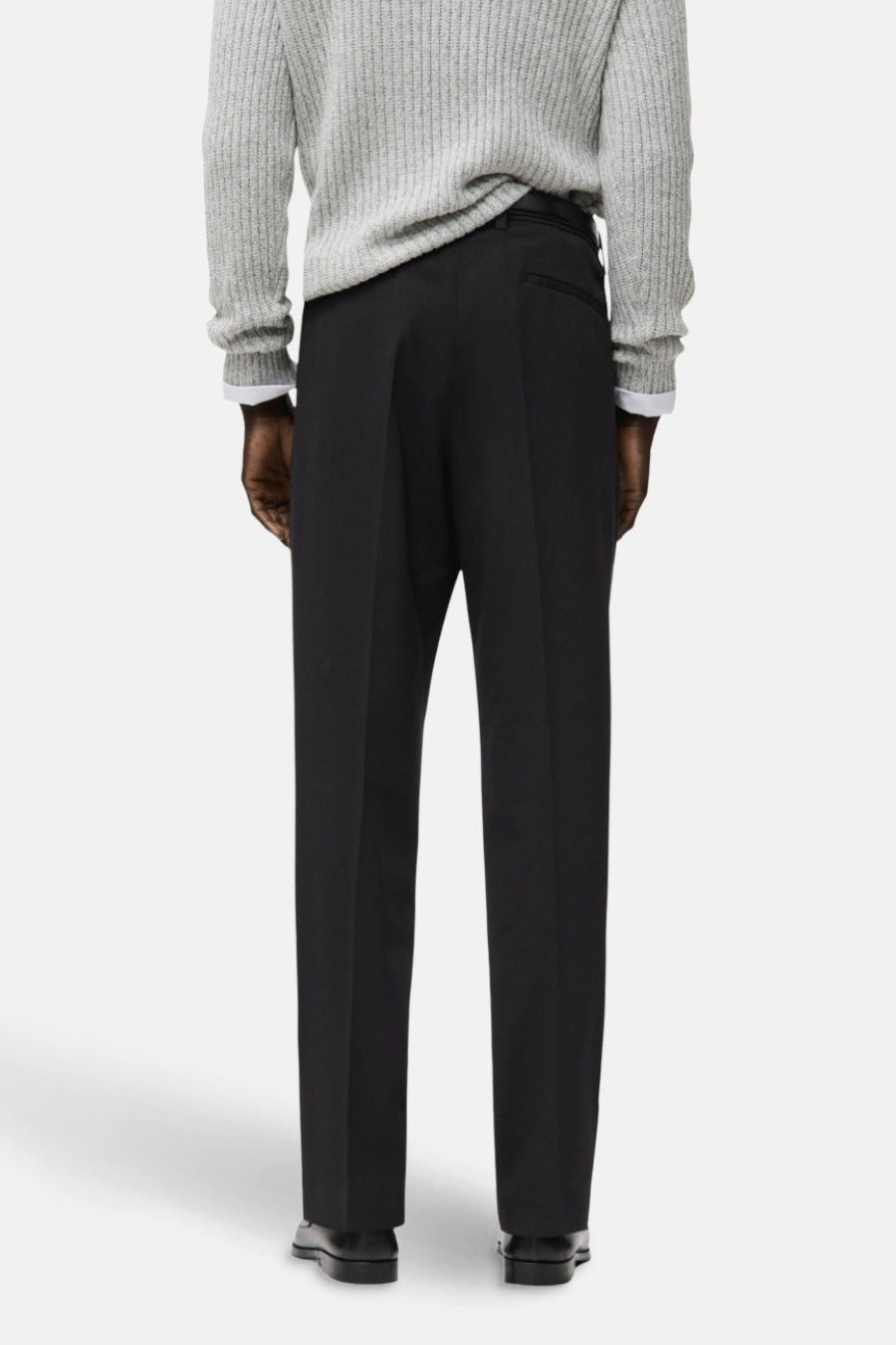 Zwarte broek van MANGO, achterkant, met een effen textuur en gecombineerd met een grijze trui.