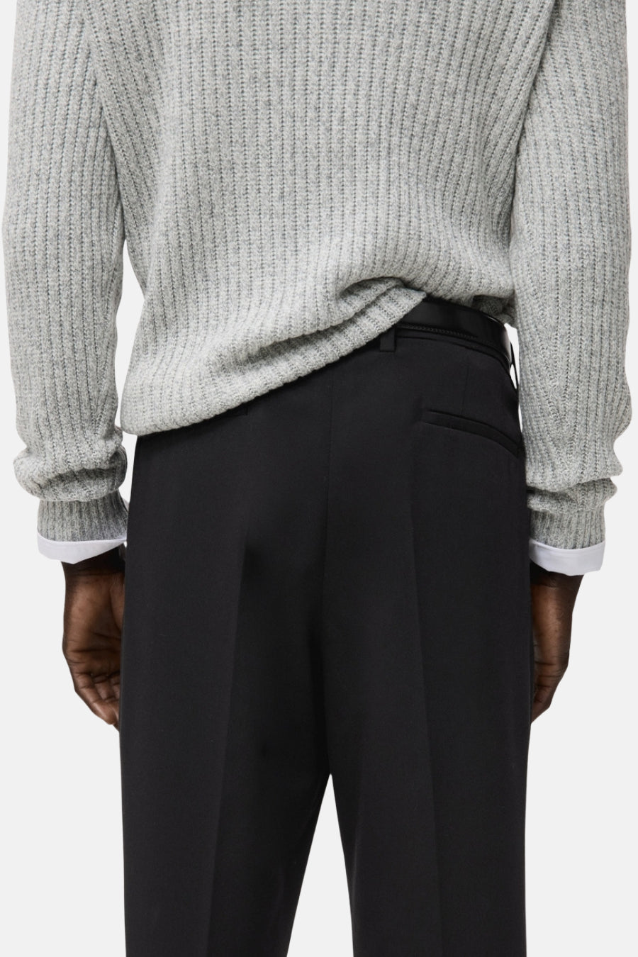 Pantalon noir de MANGO, avec une poche arrière, porté avec un pull gris et une chemise blanche.