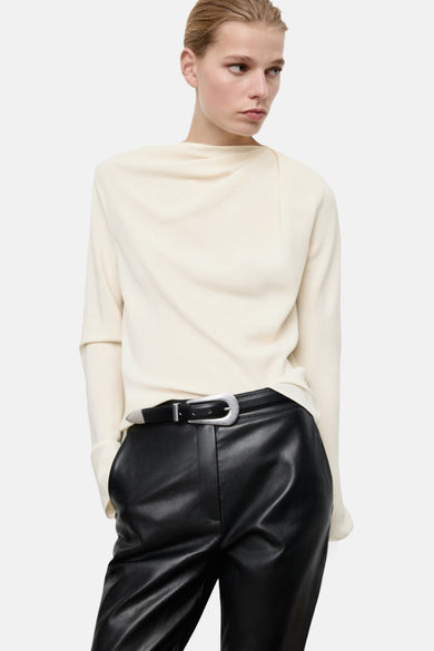 Ecru blouse met lange mouwen van MANGO, met een gedrapeerde halslijn en gecombineerd met leren broeken en een zilverkleurige riem.
