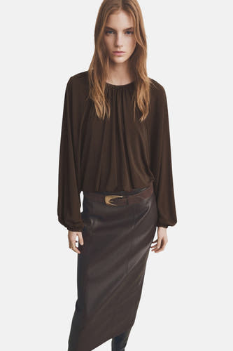 Blouse brune à longues manches de MANGO, vue de derrière, associée à une jupe en cuir.