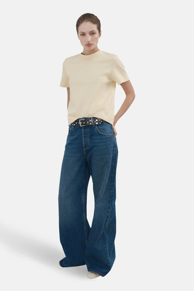 T-shirt jaune à manches courtes de MANGO, porté avec une ceinture noire à clous argentés et un jean ample.