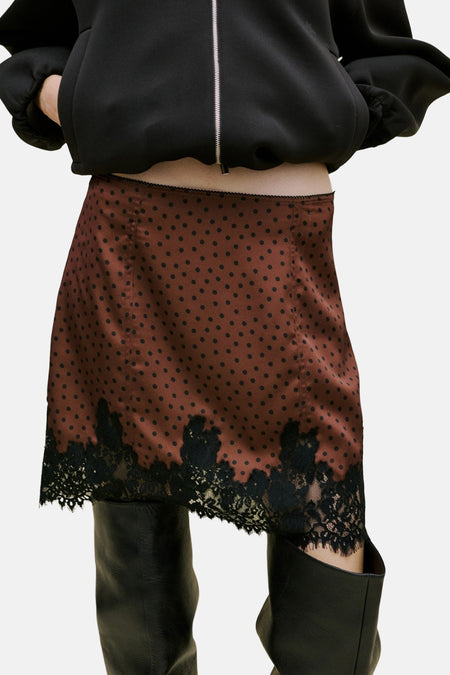 Bruine korte rok van MANGO, met zwarte stippen en zwart kant aan de onderkant, gedragen met zwarte laarzen.