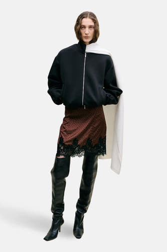 Jupe courte marron de MANGO, à pois noirs et bordure en dentelle, combinée avec un blouson bomber noir et de hautes bottes noires.