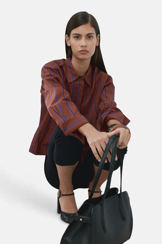 Chemise multicolore de MANGO à rayures verticales bleues, portée avec un pantalon noir et un sac à main.