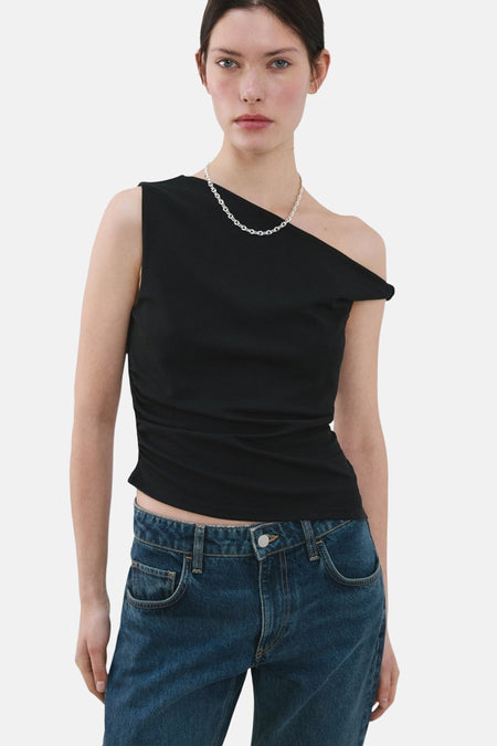 Haut noire sans manches de MANGO, avec une encolure asymétrique et portée avec une chaîne argentée et un jean bleu.