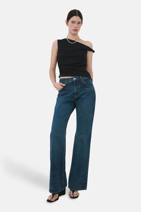 Haut noire sans manches de MANGO, avec encolure asymétrique et portée avec un collier de perles et un jean large.