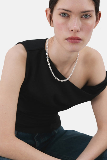 Zwarte top zonder mouwen van MANGO, met een asymmetrische halslijn en gedragen met een zilverkleurige ketting en jeans.
