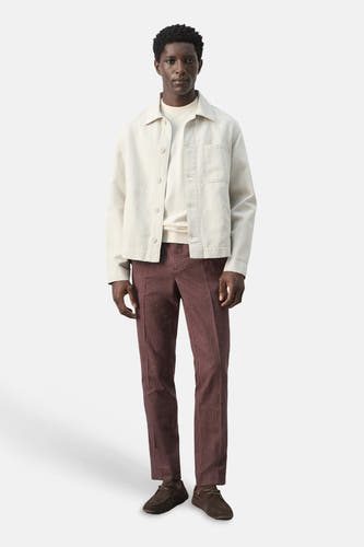 Ecru korte jas van MANGO, met lange mouwen en knoopsluiting, gedragen met bordeaux ribfluwelen broek en bruine schoenen.
