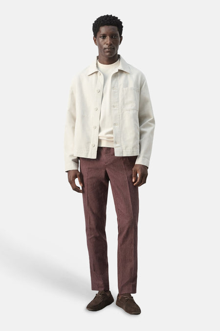 Veste courte écru de MANGO, à manches longues et fermeture boutonnée, portée avec un pantalon en velours côtelé bordeaux et des chaussures marron.