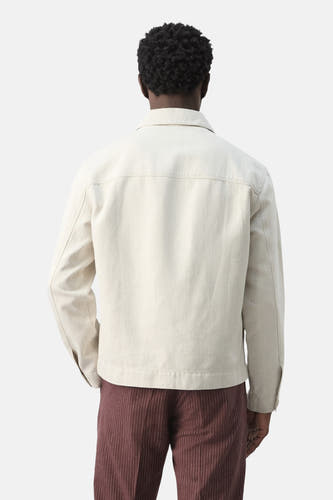 Korte ecru jas van MANGO, gezien van achteren, met lange mouwen en bruine broek.