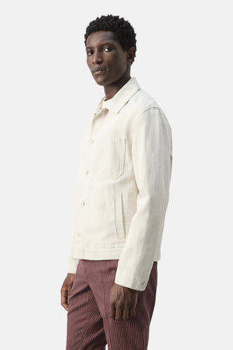 Ecru korte jas van MANGO, met lange mouwen en opgestikte zakken, gedragen met gestreepte broek.

