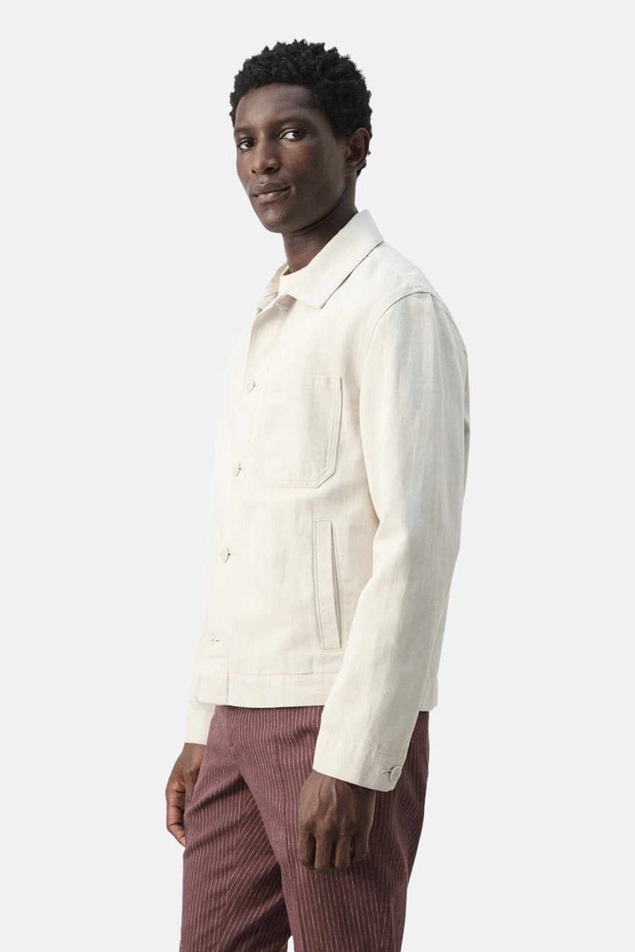 Ecru korte jas van MANGO, met lange mouwen en opgestikte zakken, gedragen met gestreepte broek.
