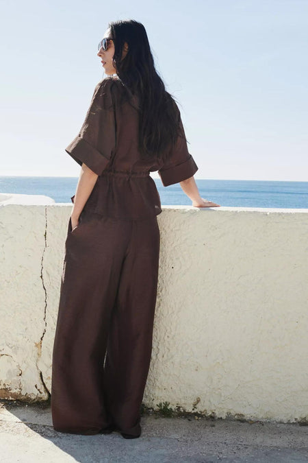 Bruine blouse met korte mouwen van MANGO, met trekkoord in de taille en opgerolde mouwen, staand aan zee.