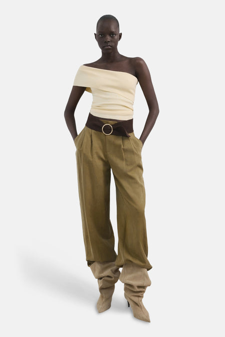 T-shirt jaune de MANGO, à une épaule et avec une ceinture marron, combiné avec un pantalon large vert et des bottes beiges.