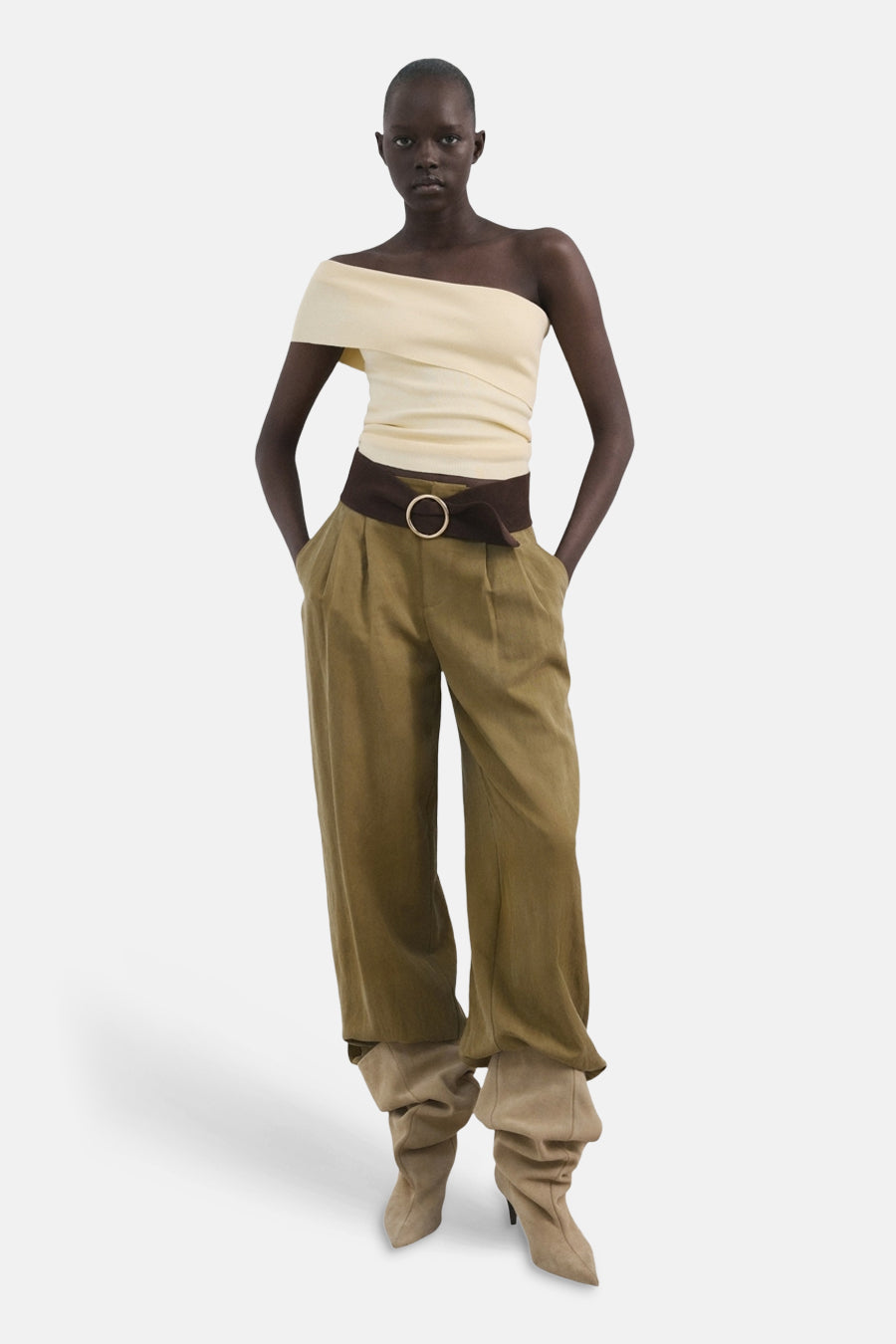 T-shirt jaune de MANGO, à une épaule et avec une ceinture marron, combiné avec un pantalon large vert et des bottes beiges.