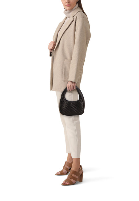 Zwarte gevlochten schoudertas van MANGO, gevormd als een halve maan, vastgehouden door een model in een beige blazer en crème broek.