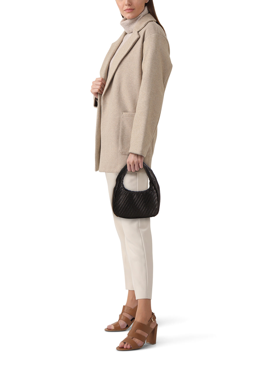 Zwarte gevlochten schoudertas van MANGO, gevormd als een halve maan, vastgehouden door een model in een beige blazer en crème broek.