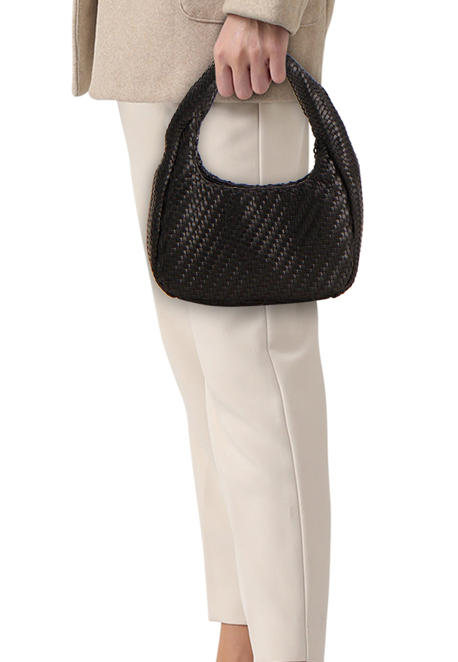 Schoudertas zwart van MANGO met gevlochten textuur, vastgehouden door een persoon in een beige jasje en crème broek.