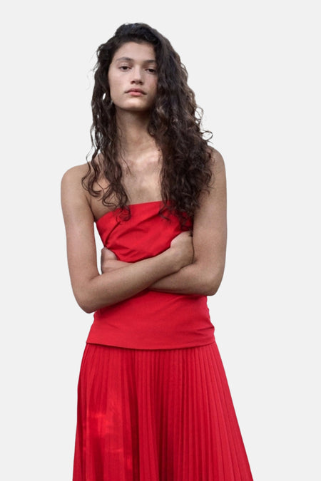 Rood strapless kleedje van MANGO met geplooide rok, gedragen door model met gekruiste armen.