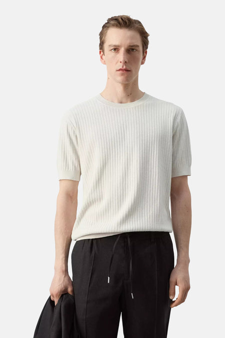 T-shirt écru à manches courtes de MANGO, avec texture côtelée, vu de dos et porté sur un pantalon noir.