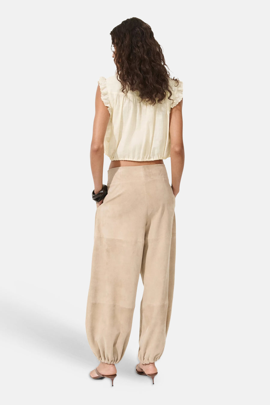 Beige mouwloze blouse met ruches aan de schouders van MANGO, achterkant weergegeven, lichte stof, model draagt beige broek en hoge hakken