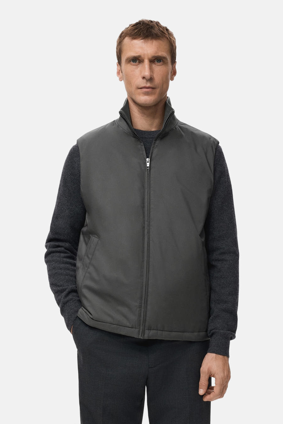 Grijze bodywarmer van MANGO, gedragen over een donkergrijze trui, met een broek in dezelfde kleur.