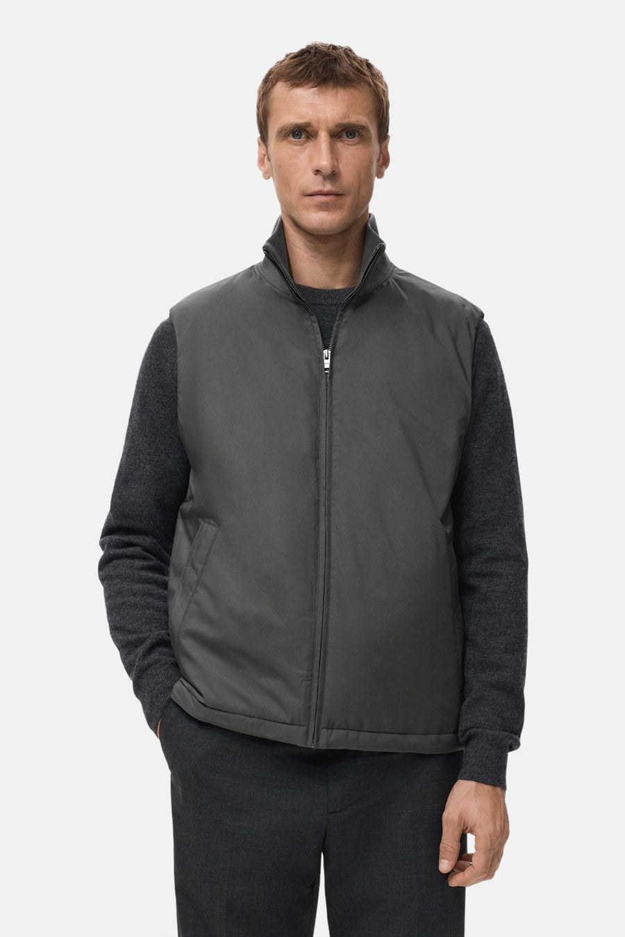 Grijze bodywarmer van MANGO, gedragen over een donkergrijze trui, met een broek in dezelfde kleur.