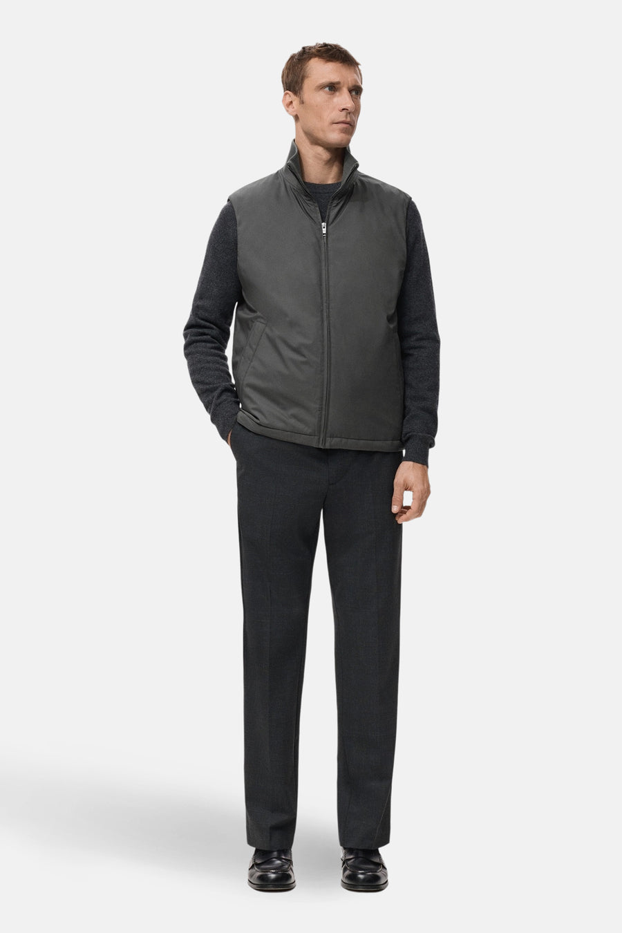 Grijze bodywarmer van MANGO, gedragen over een donkergrijze trui en pantalon, met een rits en steekzakken.