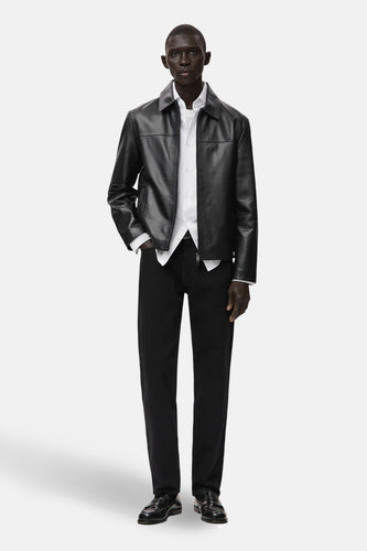 Zwarte korte jas van MANGO, met lange mouwen, gedragen over een wit overhemd en een zwarte broek, afgewerkt met zwarte schoenen.