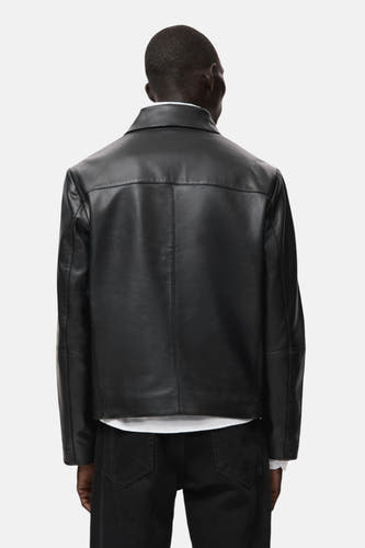 Zwarte korte jas van MANGO, rugzijde getoond, gecombineerd met een wit shirt en zwarte jeans.
