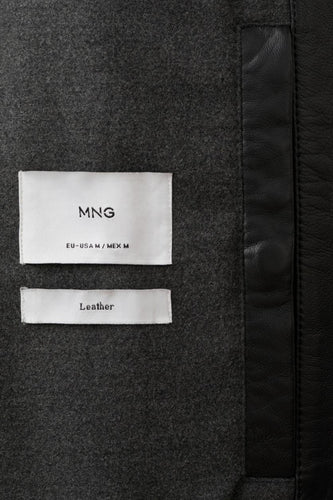 Zwarte korte jas van MANGO, met een label met "Leather" tekst en lederen accenten langs de rand.
