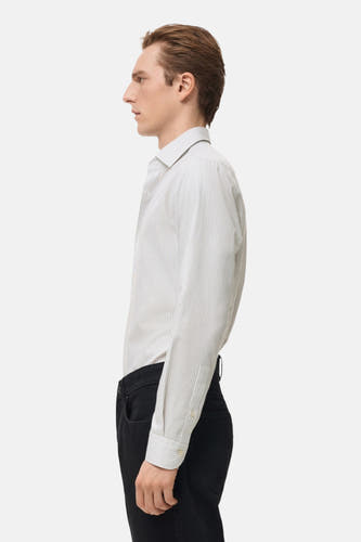 Chemise grise à manches longues de MANGO, rayée et portée avec un pantalon noir, vue de côté.
