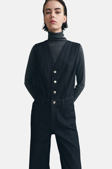 Combinaison de denim bleu marine de MANGO, avec des boutons argentés et des manches longues. Un gilet gris en dessous.