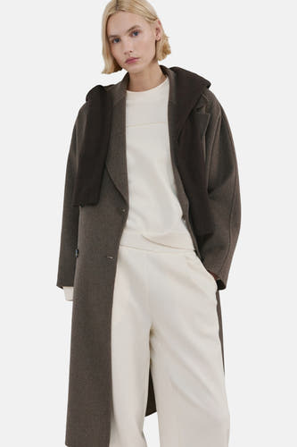 Gilet écru de MANGO, avec des manches longues et une large encolure, porté avec un pantalon crème et des baskets.