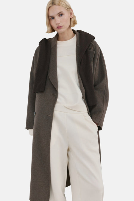 Gilet écru de MANGO, avec des manches longues et une large encolure, porté avec un pantalon crème et des baskets.