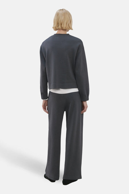 Pull-over bleu avec col rond de MANGO, vue arrière avec pantalon coordonné et cheveux blonds.