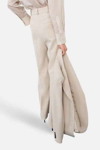 Pantalon beige de MANGO, à jambes larges et passants de ceinture, combiné avec une chemise rayée et un blazer à la main.