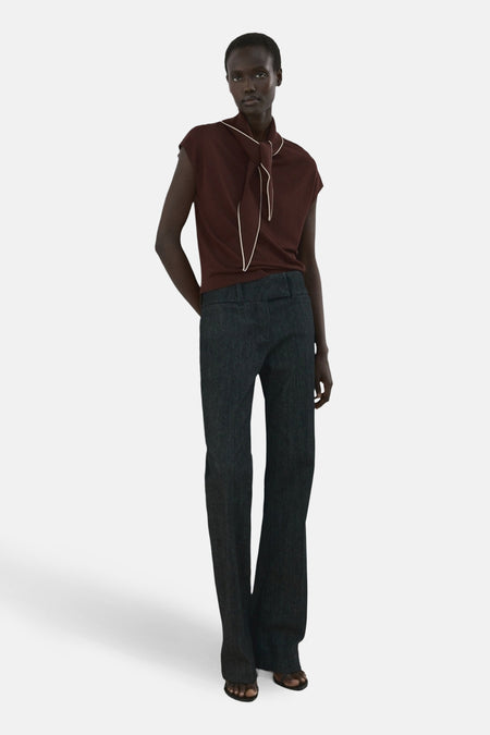 Mouwloze bruine blouse van MANGO, met witte biezen langs de halslijn en een losse knoopdetail.
