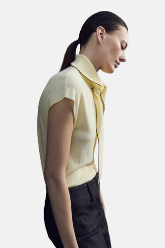 Chemisier sans manches jaune de MANGO, avec finition noire et col ouvert, combiné avec un pantalon foncé et des talons.