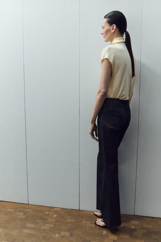Chemisier sans manches jaune de MANGO, avec un col polo et porté avec un pantalon foncé et des talons.